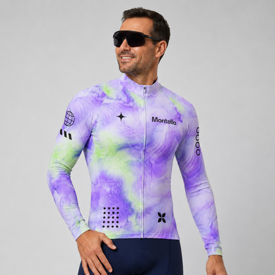 A man wearing a purple and green tie-dye long-sleeve cycling jersey with 'Montella' printed on the chest, paired with navy blue cycling shorts, against a solid gray studio background.