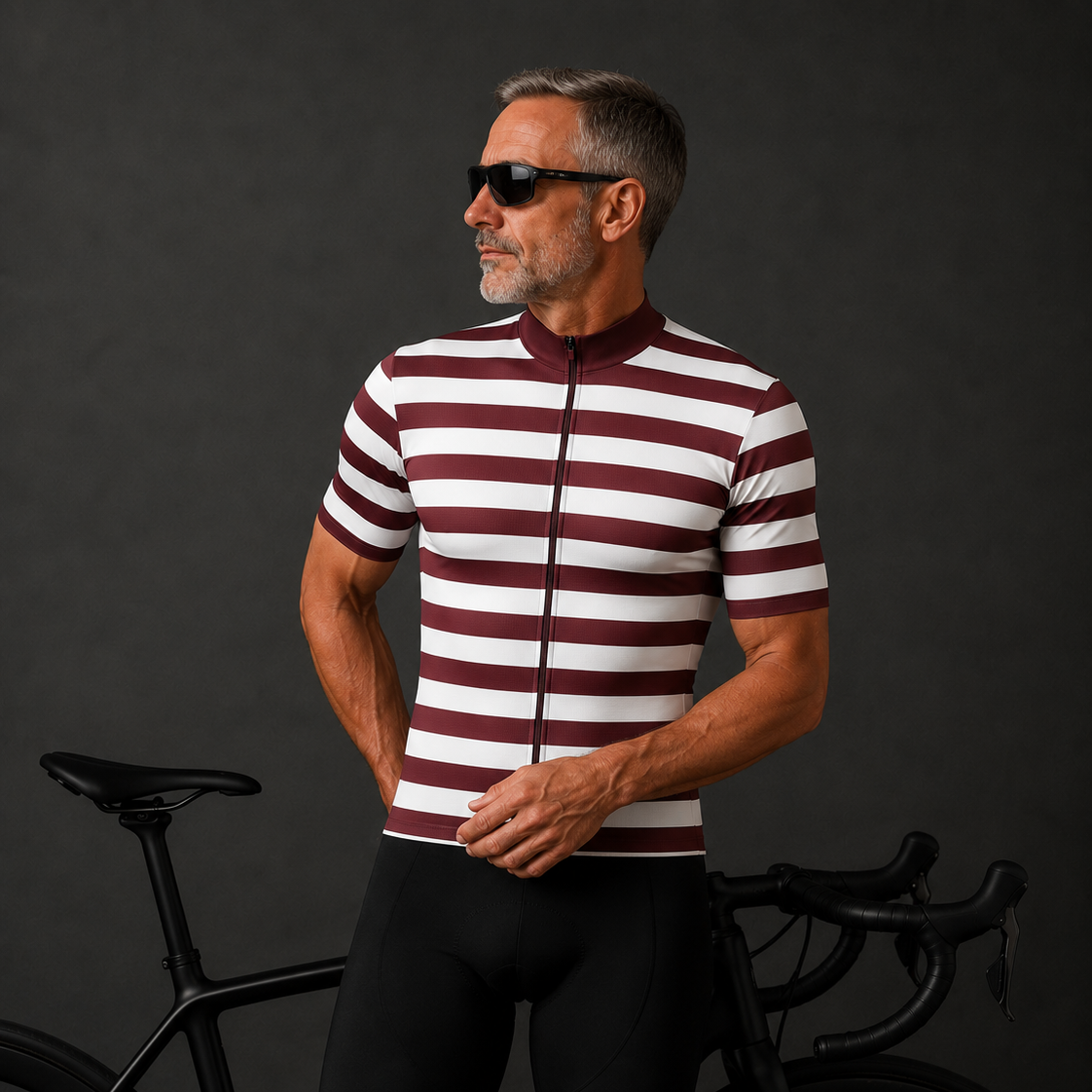 A man wearing a burgundy and white horizontally striped cycling jersey with a full-zip front, paired with black cycling shorts, standing next to a black road bicycle against a dark gray studio background.